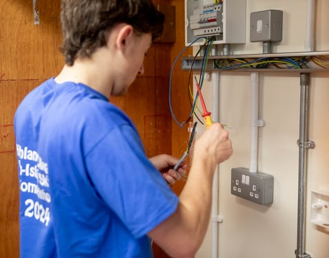 A medium close up of a person working on an electrical panel, handling wires and tools with sockets and switches visible.