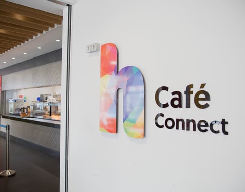 Entrance to Café Connect at Highlands College, featuring a modern interior with wooden ceiling panels, stainless steel kitchen equipment, and colourful branding.