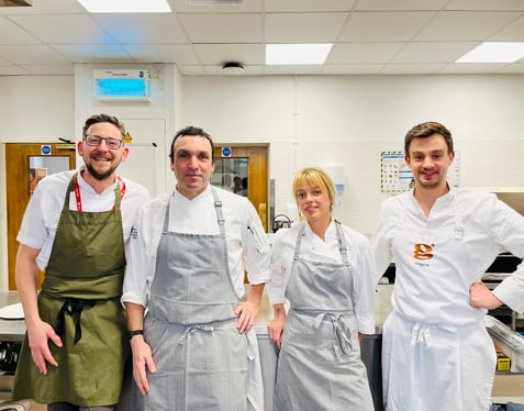 Culinary arts students at Highlands College standing in a professional kitchen wearing chef uniforms, surrounded by commercial cooking equipment.